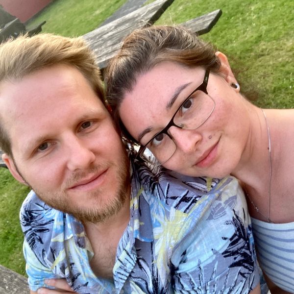 A smiling couple posing outdoors on a sunny day.