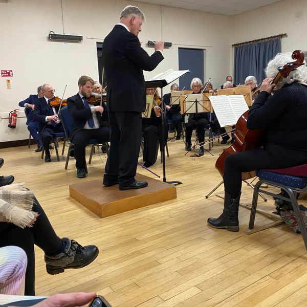 Conductor leading an orchestra during a live performance in a small indoor venue.