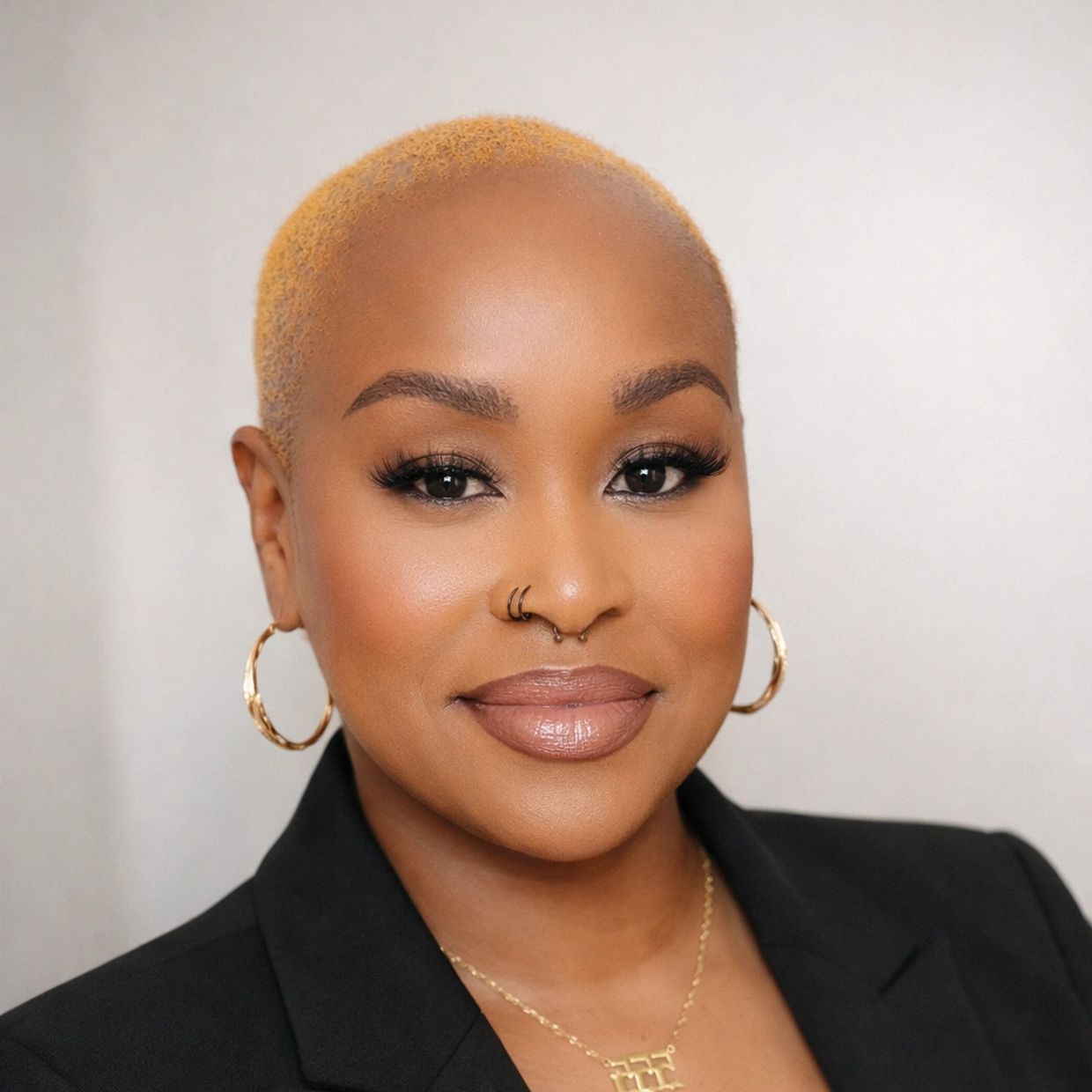 Confident woman with short blonde hair, gold hoop earrings, and nose piercings, smiling warmly.