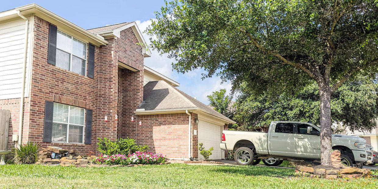 Brick house with a white truck parked beside a tree in the driveway.