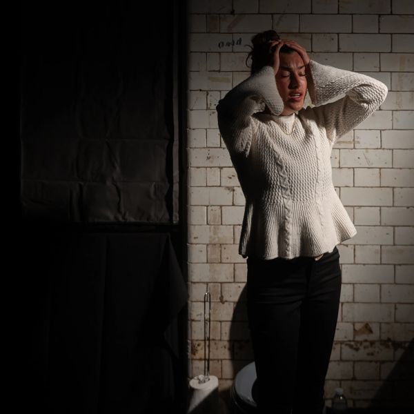 Woman in white sweater looks distressed in dimly lit, tiled room.