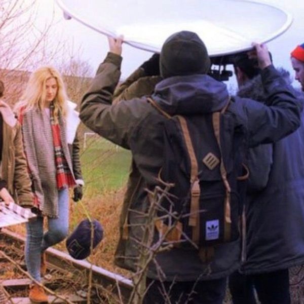 Film crew working outdoors with a young woman near a railroad track.