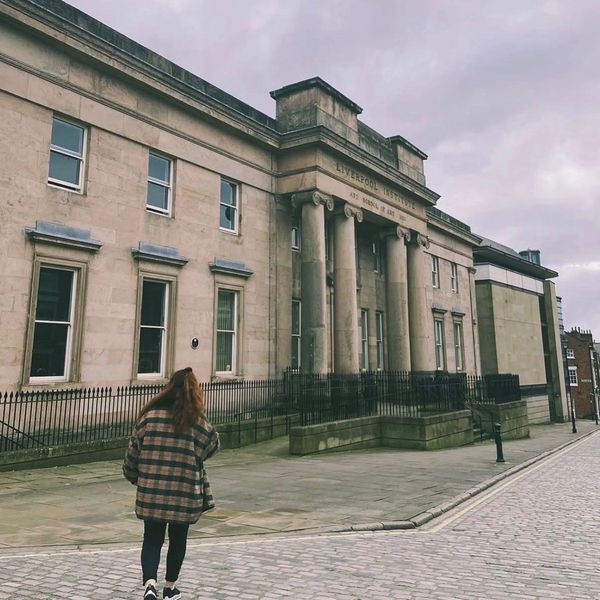 Person walking near a historic building with columns on a cloudy day.