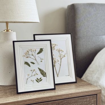 Two framed botanical prints on a bedside table next to a lamp.