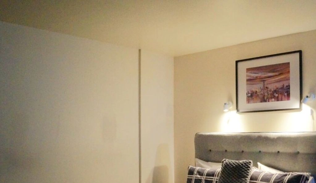 Cozy bedroom corner with a cushioned headboard and framed artwork above the bed.