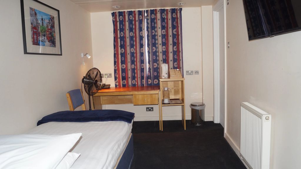 Small hotel room with single bed, desk, and colorful curtains.
