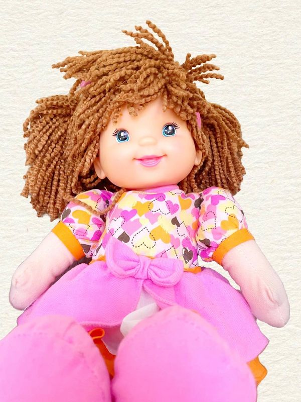 This is a child's doll that is sitting and smiling. She is wearing a pink dress with hearts on it. 