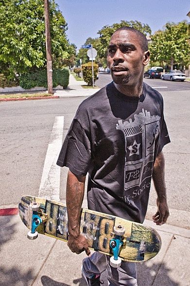 Man holding a skateboard on a sunny street corner.