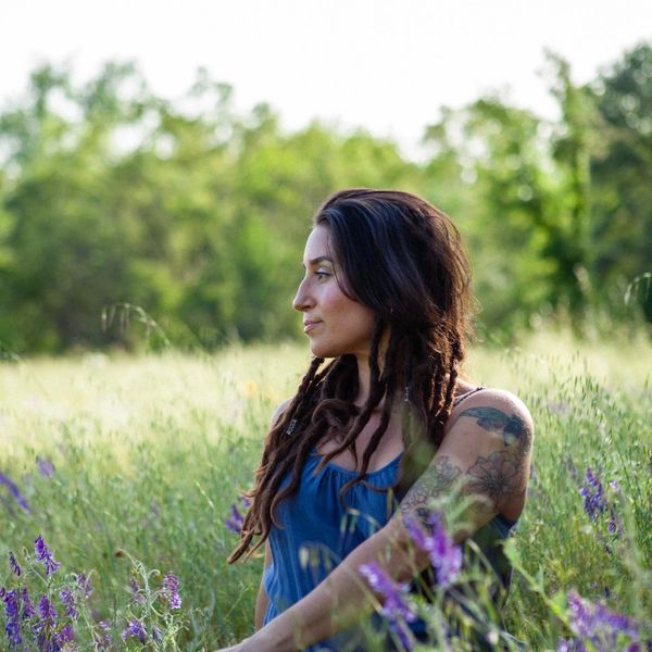 Woman with dreadlocks and tattoo in a field of wildflowers.