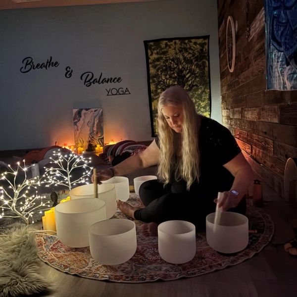Woman playing crystal singing bowls in a serene room.