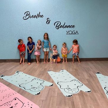 Children lined up in a yoga room with animal mats.