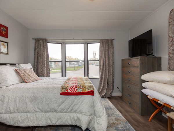 Cozy bedroom with a bay window, wooden dresser, and neatly made bed with decorative pillows.