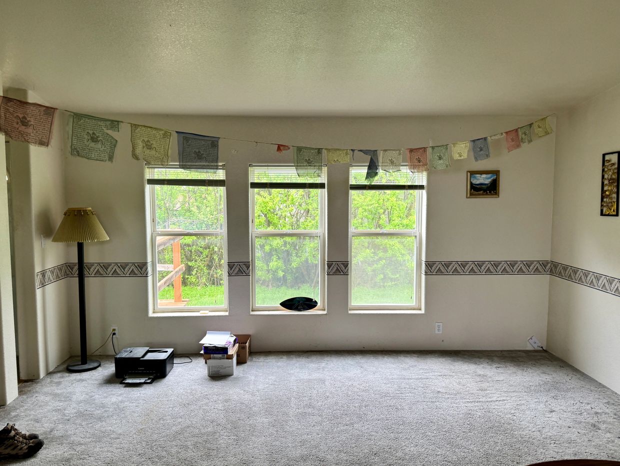 Empty room with three windows, a floor lamp, printer, and prayer flags.