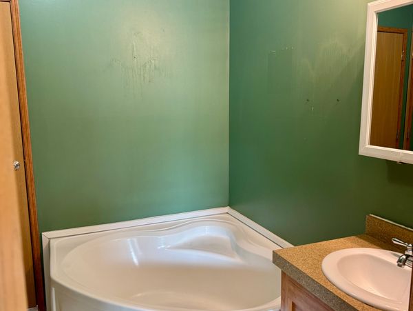 A corner bathtub in a green-walled bathroom with a sink and mirror.