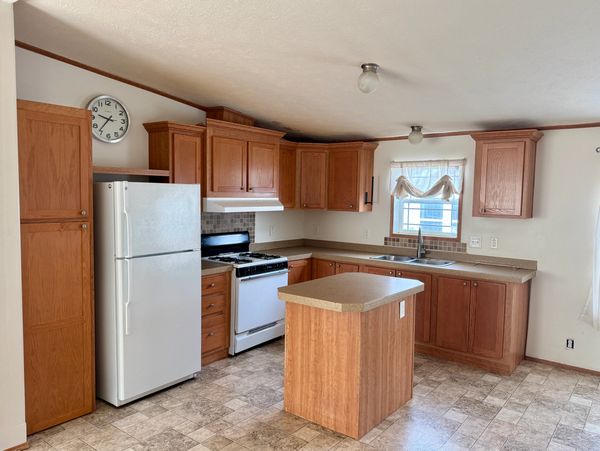 Bright kitchen with wooden cabinets, a white refrigerator, and a central island.