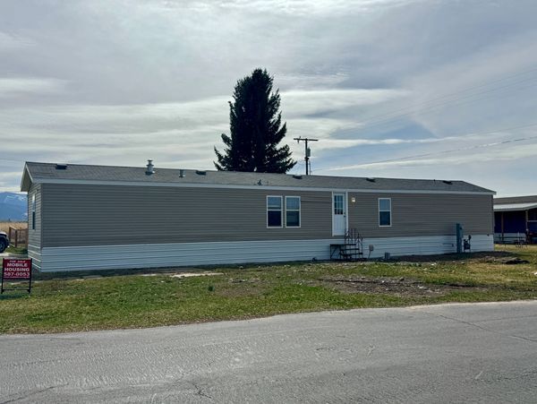 Single-story mobile home in a rural setting with a cloudy sky.