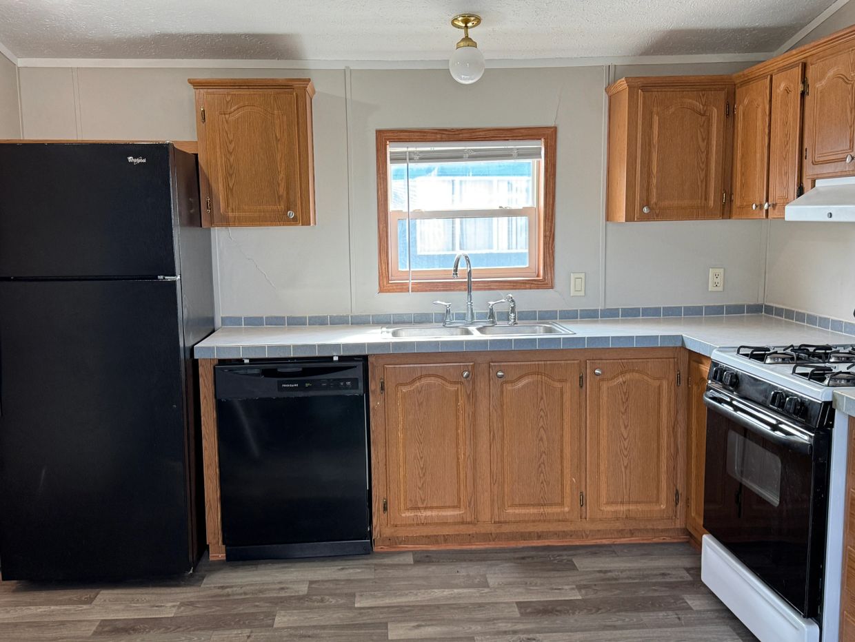 Simple kitchen with wooden cabinets and black appliances under natural light.