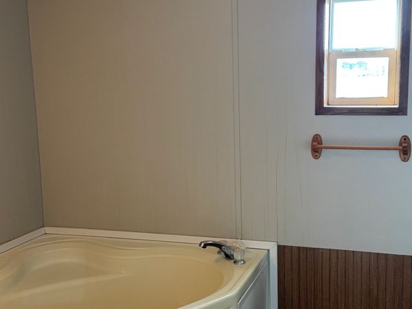 Bathtub corner with faucet next to a small window and towel rack.