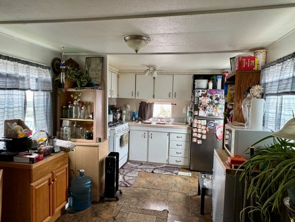 Cozy kitchen with white cabinets, a fridge covered in magnets, and natural light from windows.