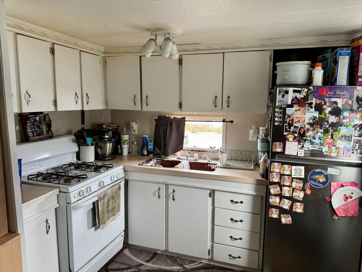 Cozy kitchen with white cabinets, stove, sink, and a fridge covered in family photos and magnets.