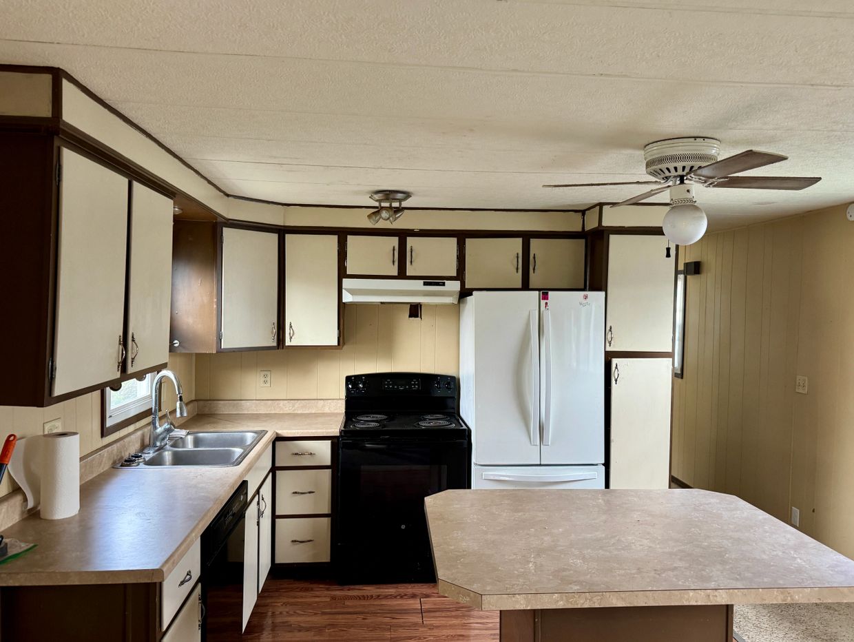 Compact kitchen with beige cabinets, black appliances, and a ceiling fan over an island.