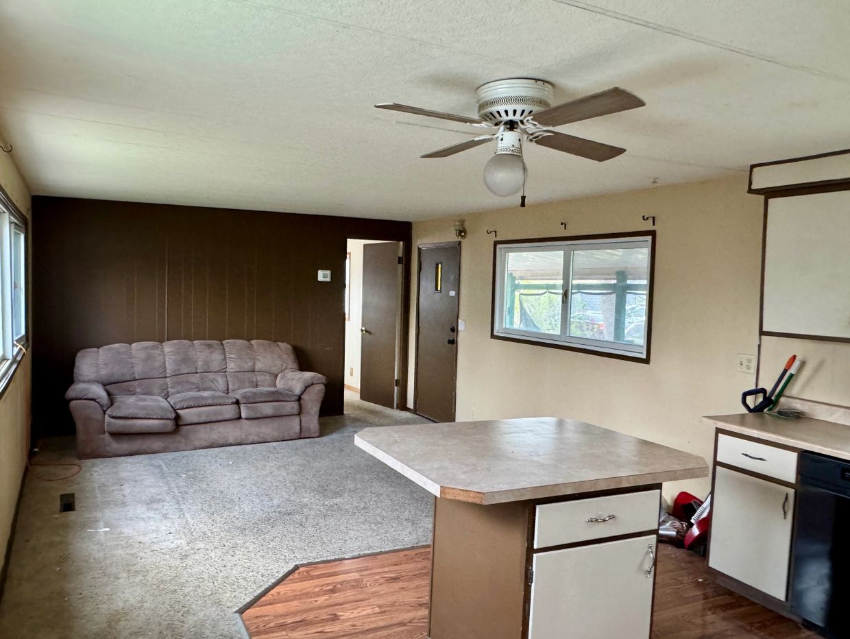 Cozy living room with a brown couch, ceiling fan, and kitchen island.