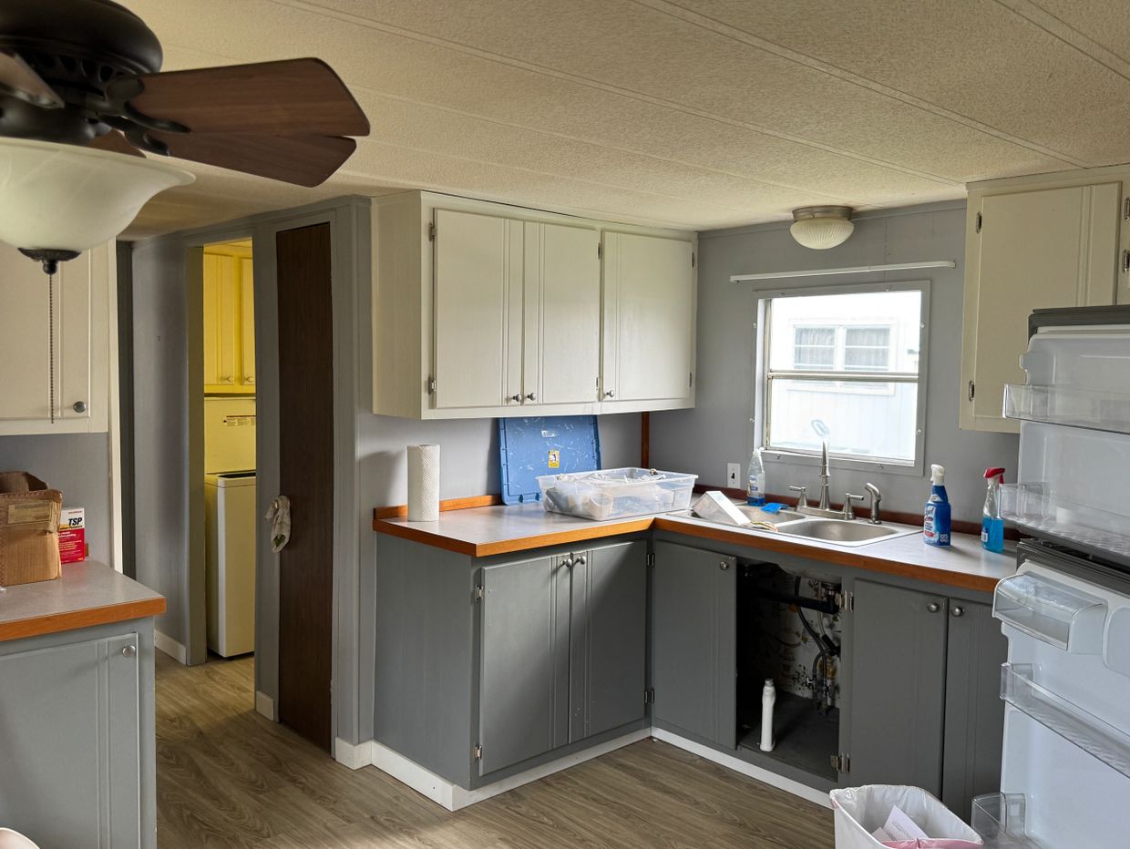 Kitchen with gray and white cabinets, a window, and items on countertops.