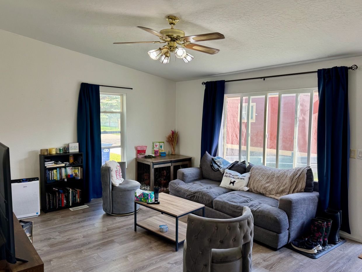 Cozy living room with gray furniture, blue curtains, and a ceiling fan.