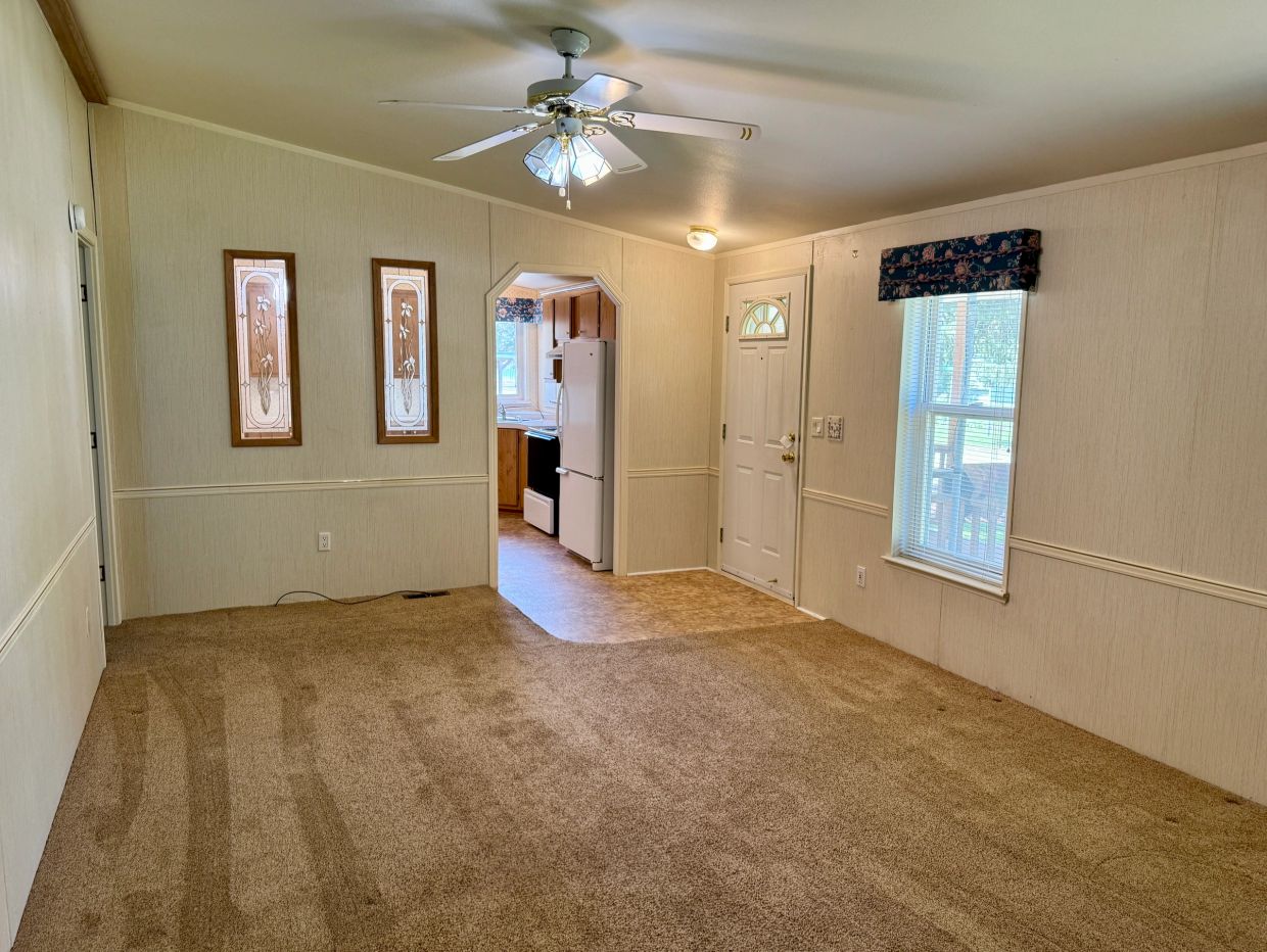 Empty living room with carpet and ceiling fan.