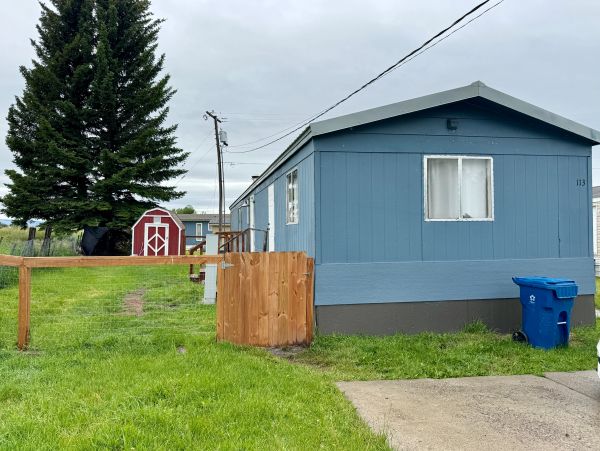 Blue mobile home with green lawn and red shed.