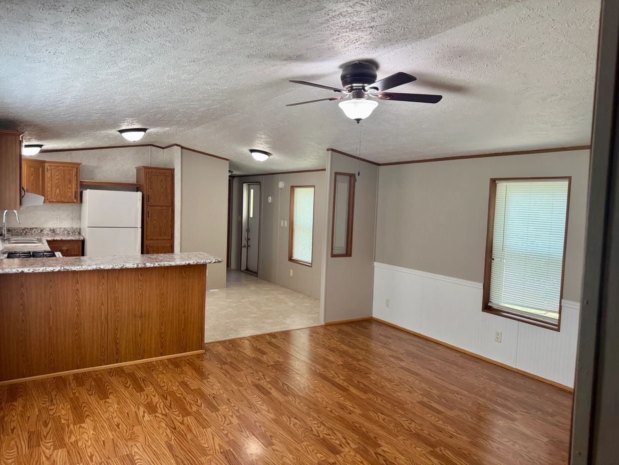 Empty room with wooden floor and kitchen area.