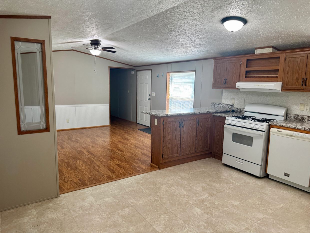 Empty kitchen and living area with wood and tile flooring.
