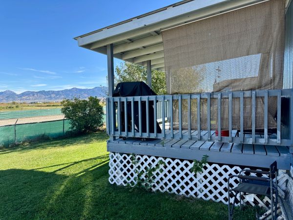Covered grill on a wooden porch with green lawn and mountains in the distance.