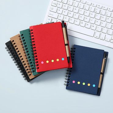 Colorful spiral notebooks with pens beside a computer keyboard.