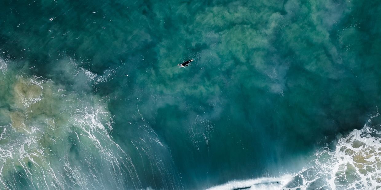 A lone surfer paddles in the vast ocean surrounded by waves.