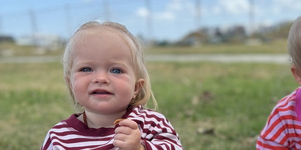 Toddler in a striped shirt outdoors on a grassy field.