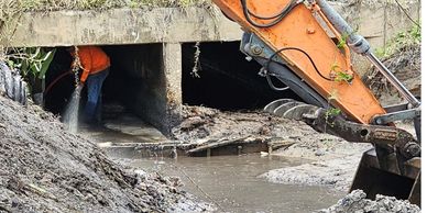 Excavator and worker cleaning a muddy drainage tunnel.