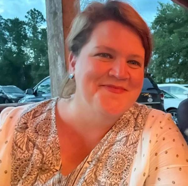 Smiling woman in patterned blouse outdoors during evening.