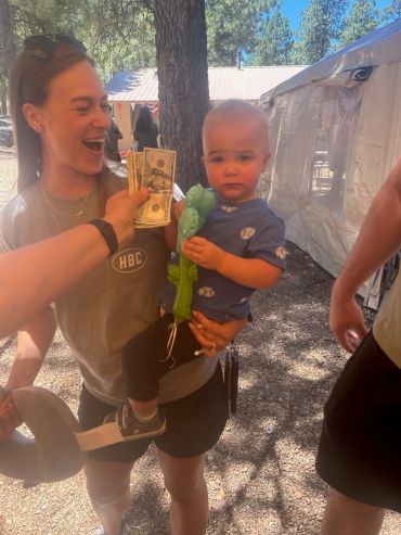 Woman smiling, holding child who holds a toy, with money being displayed.