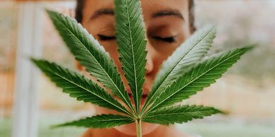 A woman holding up a marijuana leaf.