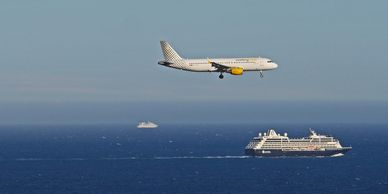 A passenger airplane flying over the ocean near two ships.