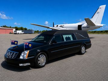 A black hearse parked near a small private jet on a sunny runway.