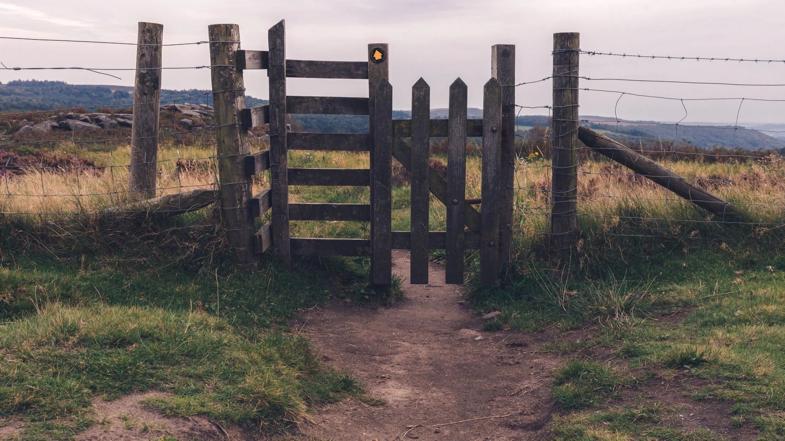 Rustic wooden gate along a countryside path with rolling hills in the background.