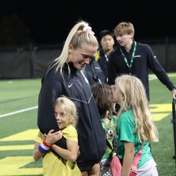 Woman in sportswear happily interacting with children on a field at night.