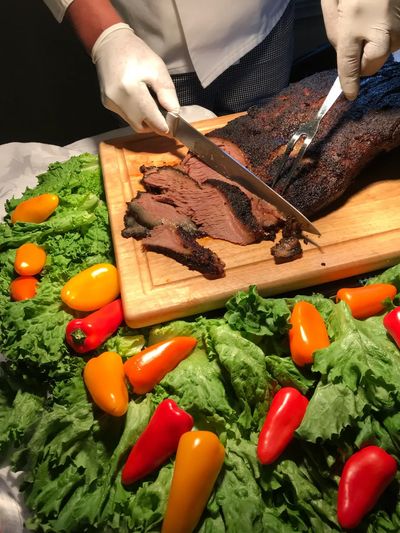 Chef slicing smoked brisket on a wooden board with fresh vegetables.
