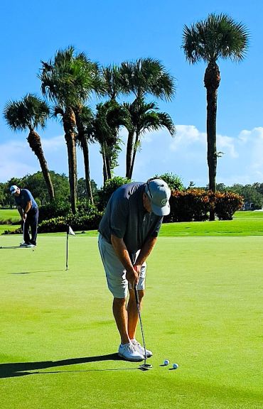 Two men playing golf on a sunny day with palm trees in the background.