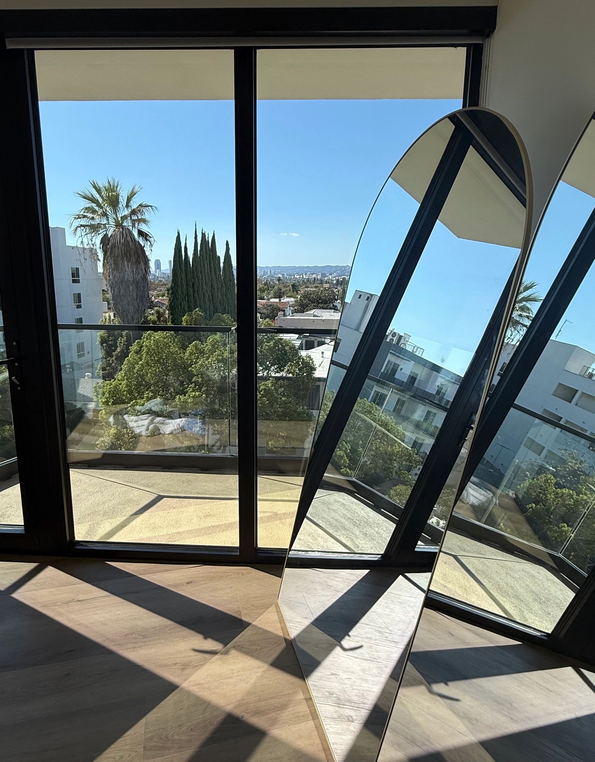 View of cityscape through glass doors with a standing mirror reflecting the scene.