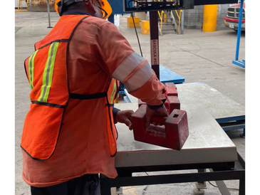 Worker in safety gear handling heavy red weights on a metal table.