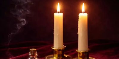 Two lit candles and a smoking bottle on a dark background.