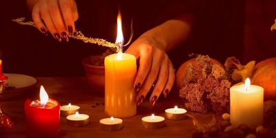 Hands lighting candles with a sage stick in a warm, cozy setting.